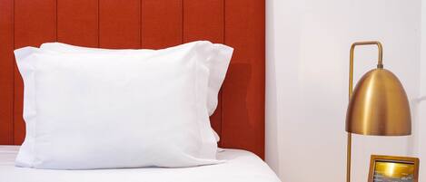 A neatly made bed with a white pillow and a gold lamp beside it.