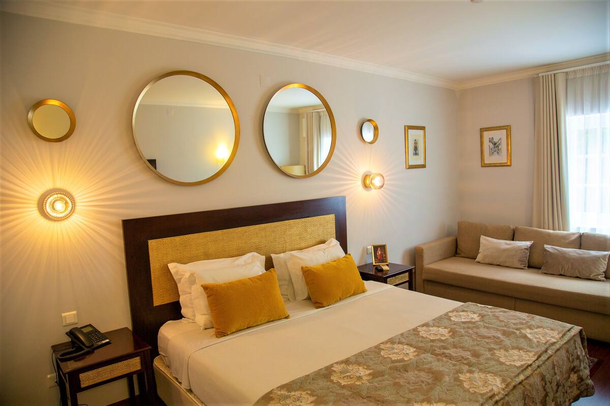 Une chambre d’hôtel avec un grand lit, un canapé et plusieurs miroirs fixés au mur.