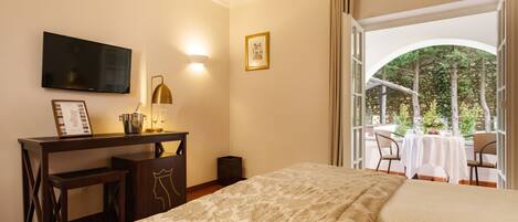 Habitación de hotel con cama, escritorio con lámpara, televisión y vista a un patio exterior con mesa y sillas.