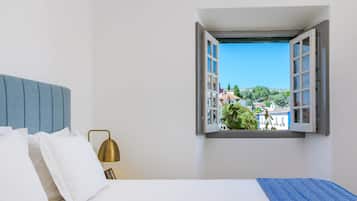 Quarto com uma cama, mesa de cabeceira, luminária e janela com persiana aberta.