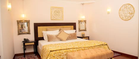 A bedroom with a large bed, a bench, a patterned rug, and decorative wall sconces.