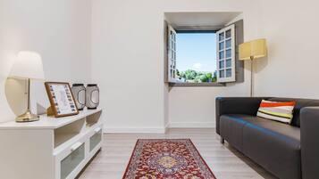 A modern living room with a sofa, a lamp, a small table with a picture frame, a patterned rug, and a window with an open shutter.