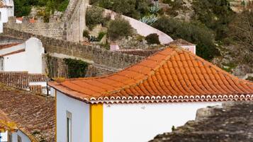 Vista de una antigua pared de piedra con una torre, sobre un pueblo con edificios de tejados de terracota y un cartel que indica un restaurante.