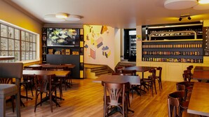 Een restaurant met houten tafels en stoelen, een bar met flessen op de planken, en een groot televisiescherm aan de muur.
