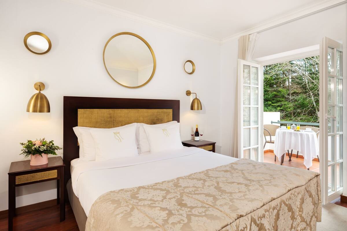 Une chambre d’hôtel avec un grand lit, deux tables de chevet, une commode, un miroir et une vue sur l’extérieur.