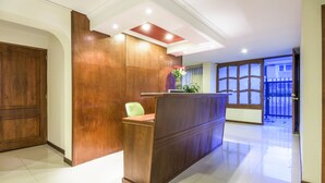 A reception area with a wooden reception desk, a green chair, and a potted plant. - Hotel Portofino (Bogotá)