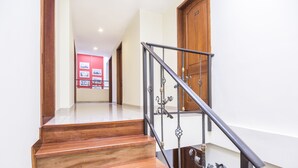 A wooden staircase with metal railings leading to a room with a wooden door and a red wall with framed pictures. - Hotel Portofino (Bogotá)