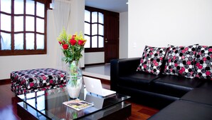A modern living room with a glass coffee table, a black leather sofa, and a white laptop. - Hotel Portofino (Bogotá)