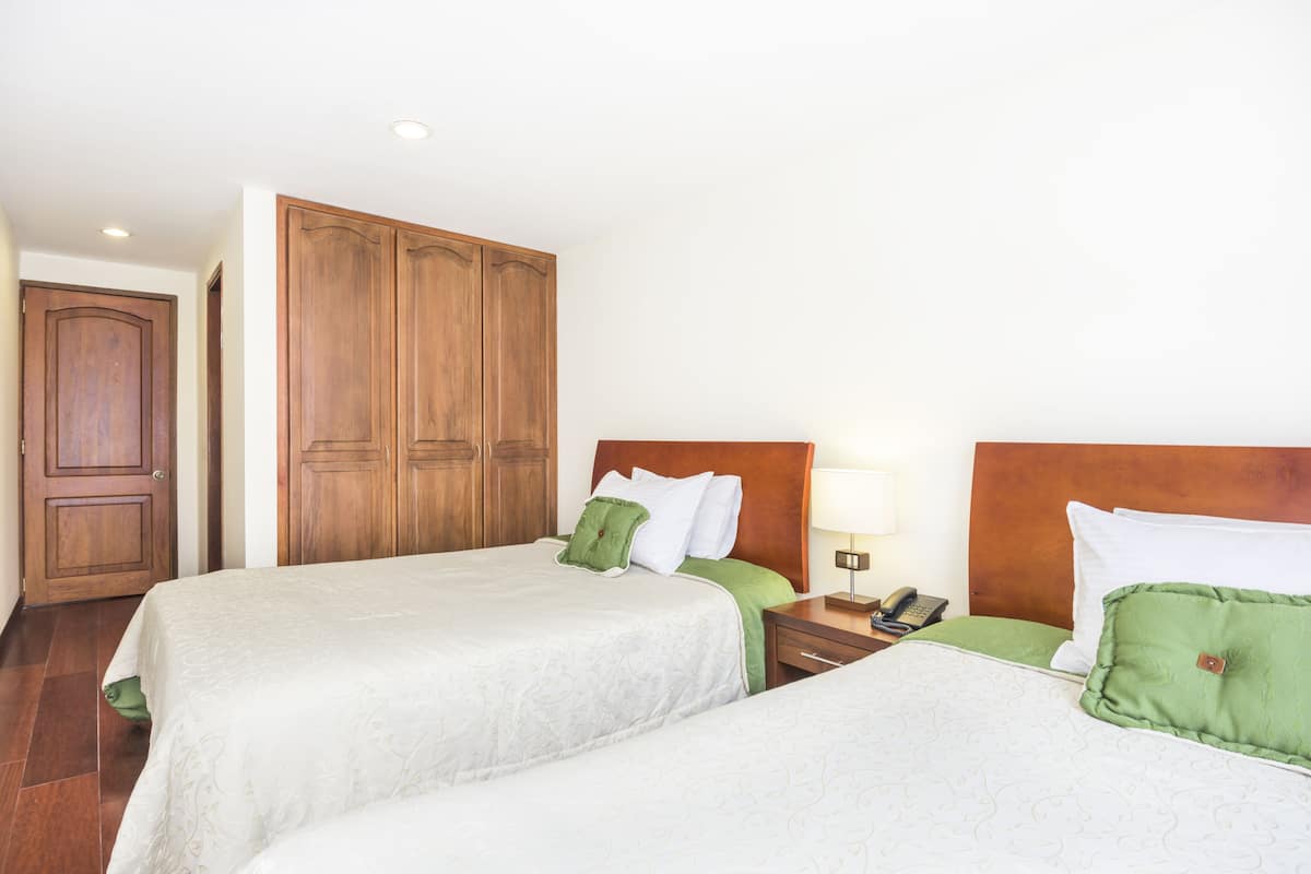 Une chambre d’hôtel avec deux lits, des armoires en bois, une table de chevet avec une lampe et un téléphone.