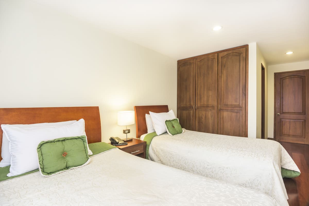 Une chambre d’hôtel avec deux lits, des têtes de lit en bois, une table de chevet avec une lampe et une armoire.