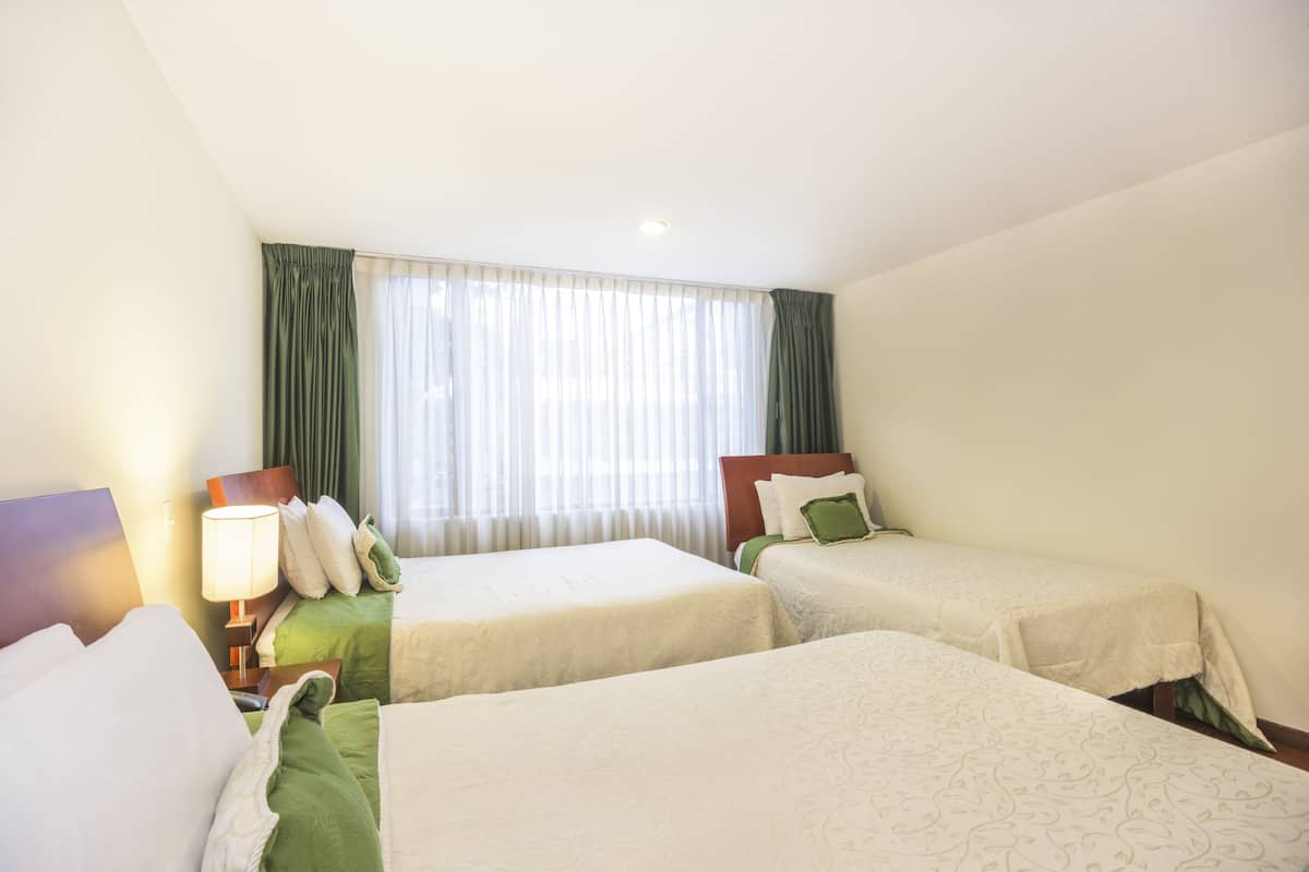 Une chambre d’hôtel avec deux lits simples, une table de chevet avec une lampe et une fenêtre avec des rideaux.