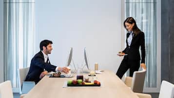 Una sala de conferencias moderna con una mesa larga, dos sillas y una persona sirviendo comida.