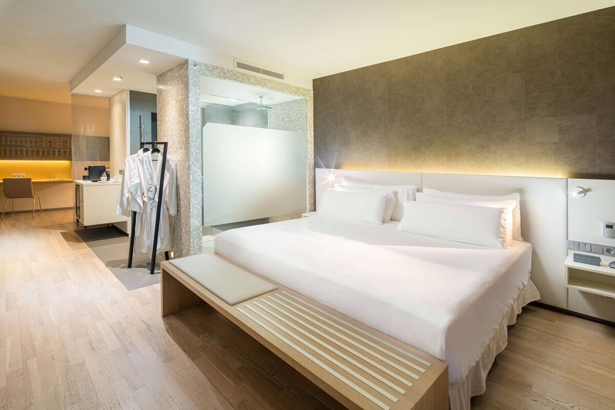 A modern hotel room with a large bed, bedside tables, a desk, and a shower area.