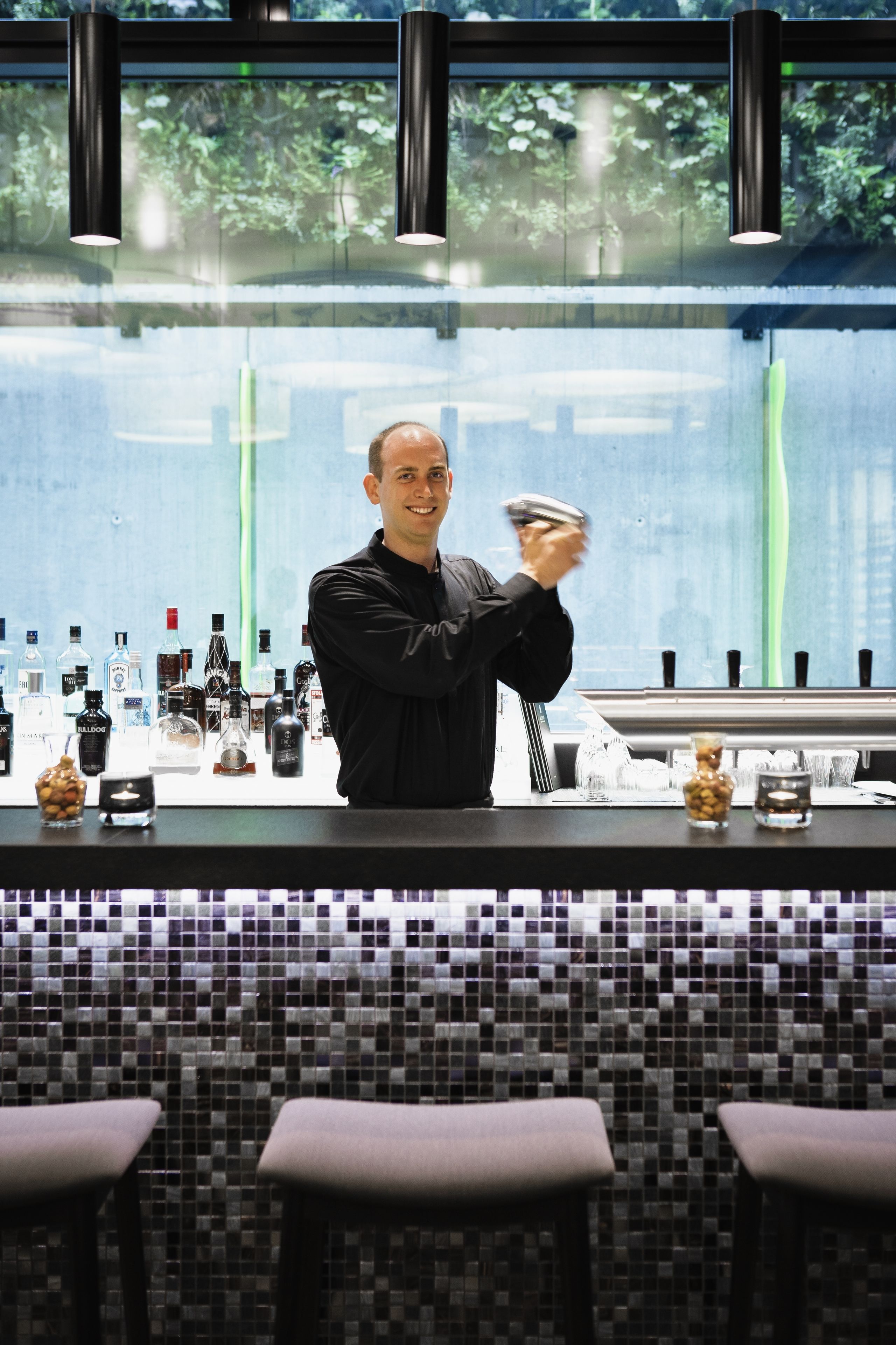 Eine Bar mit Barkeeper, verschiedenen Flaschen, Gläsern und einer gefliesten Rückwand.