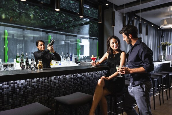 Un área de bar moderna con un camarero, una mujer sentada y un hombre de pie.