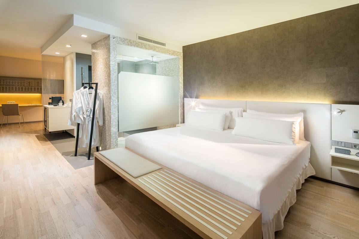 A modern hotel room with a large bed, bedside tables, a desk, and a shower area.