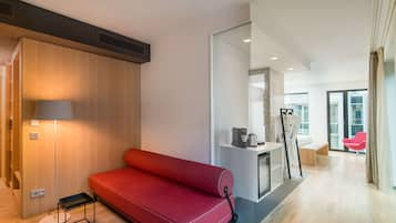 A modern hotel room with a red sofa, a small table with a lamp, and a large mirror.