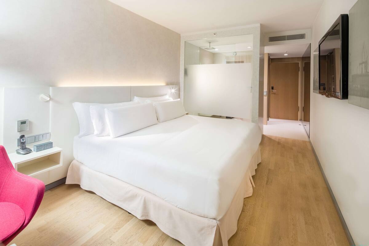 A modern hotel room with a large bed, bedside tables, a flat-screen TV, and a mirror.