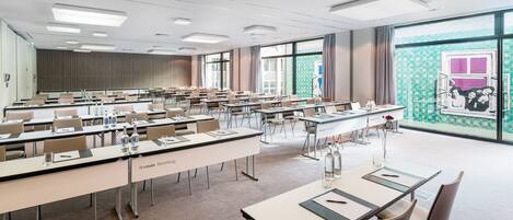Un salón de conferencias con varias mesas y sillas, tarjetas de identificación y un amplio ventanal con vista a un edificio.
