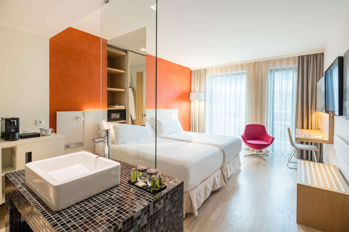 A hotel room with a large bed, a smaller bed, a bathtub, a desk, a chair, and a TV.