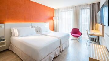 A hotel room with two beds, a desk, a chair, and a TV.