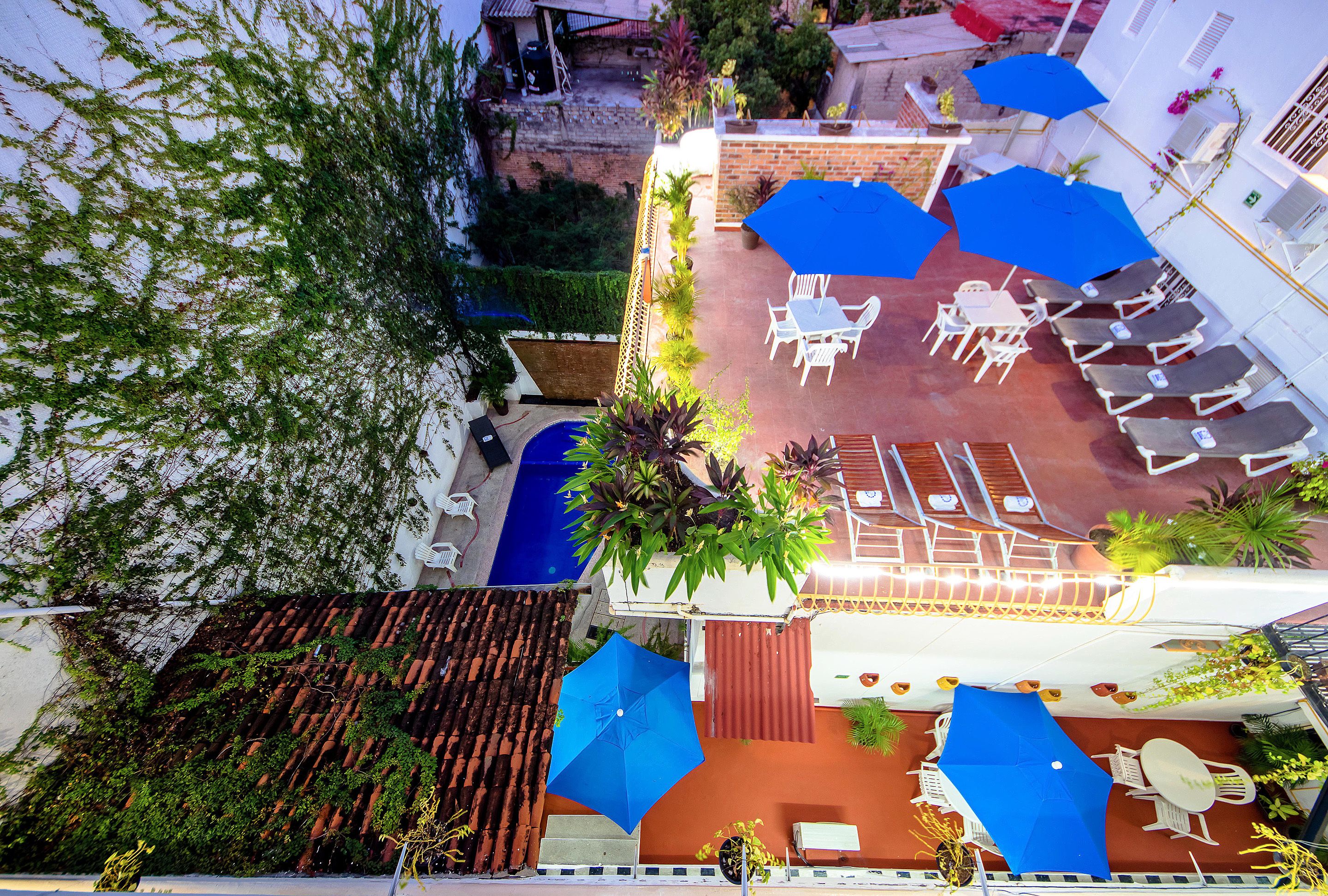 Eine Terrasse im Freien mit weißen Stühlen und Tischen, blauen Sonnenschirmen und Topfpflanzen.