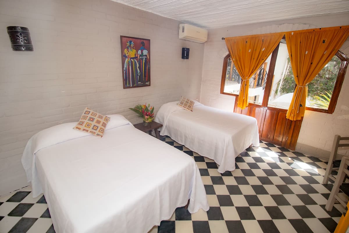 Una habitación con dos camas individuales, piso a cuadros, un cuadro en la pared y una ventana con cortinas.