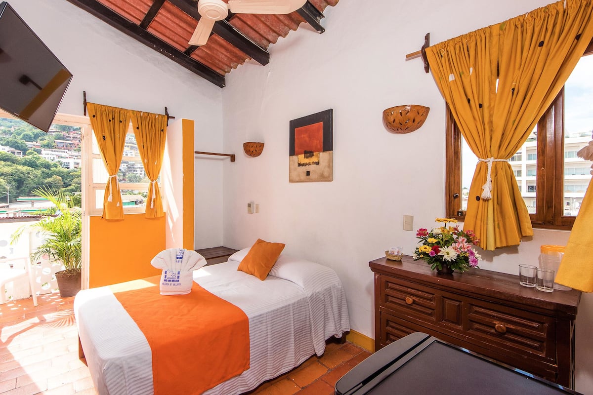 Habitación de hotel con cama, cómoda, televisión y ventana con cortinas.