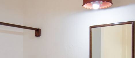 Une salle de bain avec un lavabo blanc, une étagère en bois, un miroir et un luminaire fixé au mur.