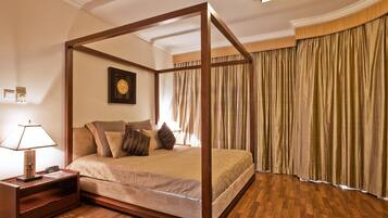 A four-poster bed with a wooden frame, a bedside table with a lamp, and a large window with curtains.