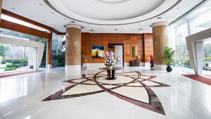 Eine großzügige Lobby mit einem zentralen, geometrischen Bodenmuster, großen Säulen und einer modernen Decke mit konzentrischen Kreisen.