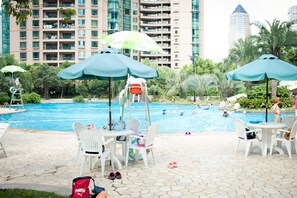 Ein Poolbereich mit Sitzgelegenheiten und Sonnenschirmen, umgeben von einem Schwimmbad und hohen Gebäuden im Hintergrund.