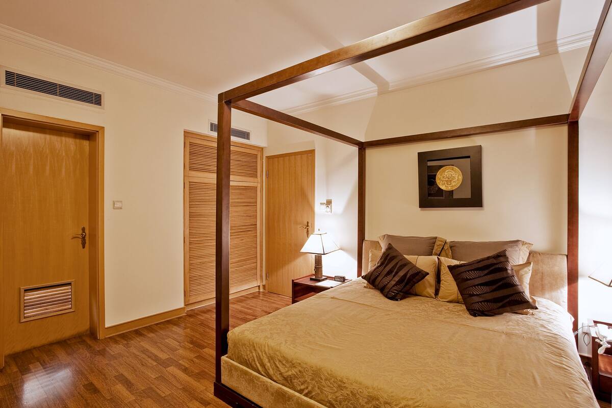 Ein Bett mit Baldachin, ein Nachttisch mit Lampe sowie ein gerahmtes Bild an der Wand.