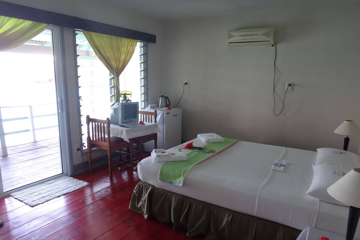 A hotel room with a bed, a desk with a computer, an air conditioner, and a view of the outside.