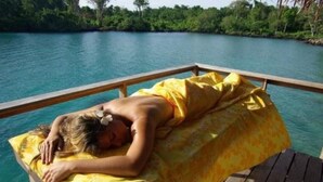 Una persona sdraiata su un pontile di legno con un asciugamano giallo, con vista su un corpo d'acqua.
