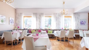 A restaurant with multiple tables and chairs, large windows with curtains, and a chandelier. - Alte Post (Fulpmes)
