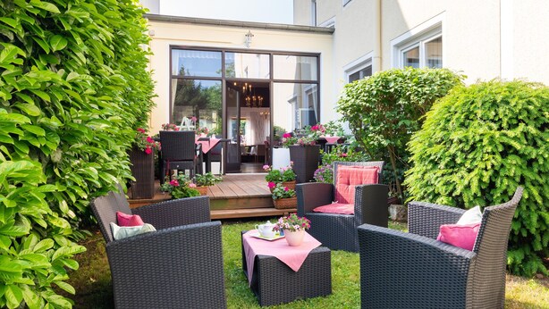 A patio area with wicker furniture, a table with a pink tablecloth, and potted plants. - Alte Post (Fulpmes)