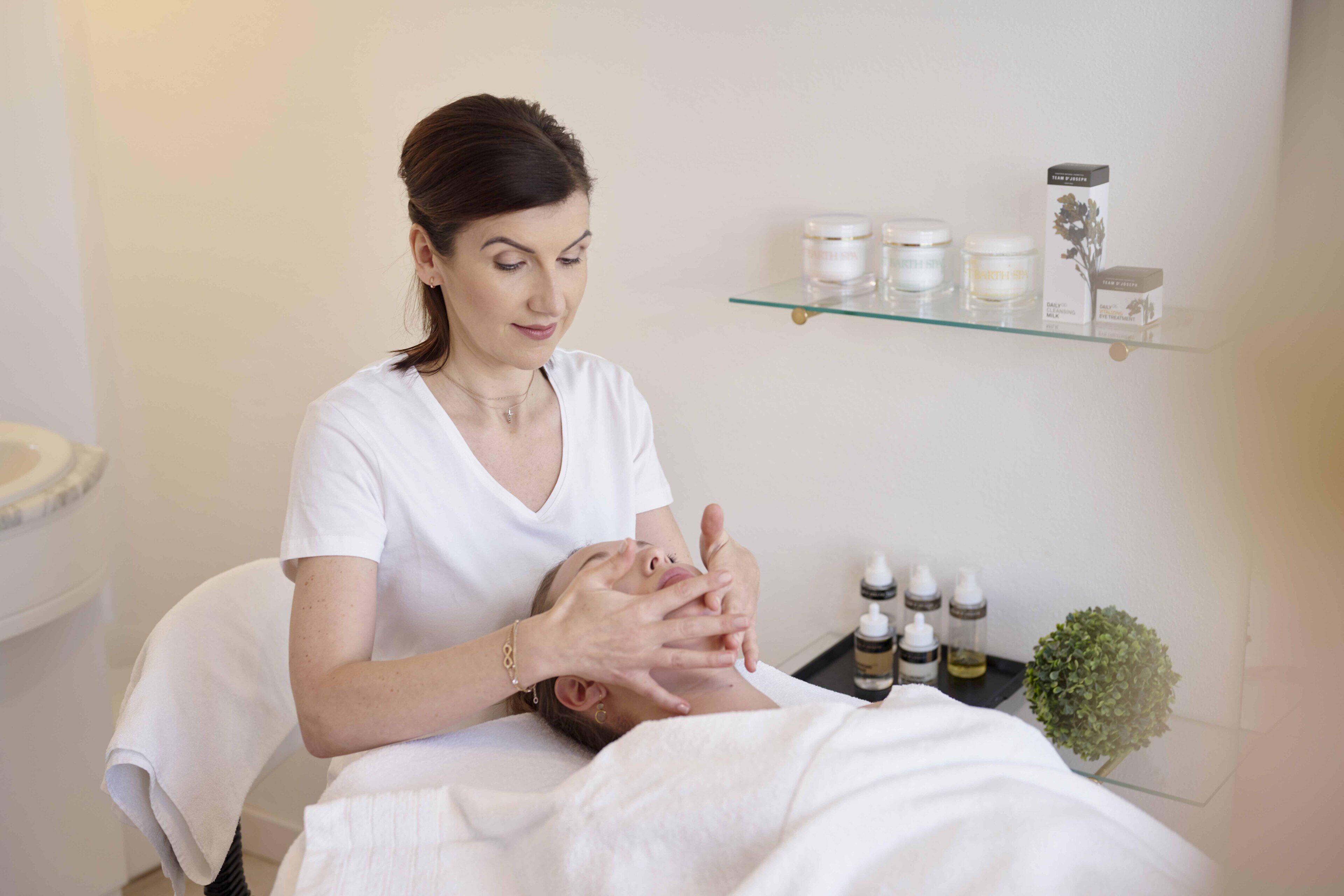A person receiving a facial treatment in a room with a glass shelf displaying various skincare products.