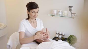 A person receiving a facial treatment in a room with a glass shelf displaying various skincare products.
