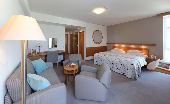 A hotel room with a bed, two armchairs, a desk, a lamp, and a round mirror.