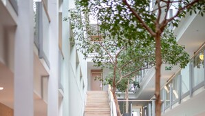 A modern indoor atrium with a central staircase, potted plants, and seating areas.