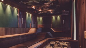 A sauna with wooden benches and a stone floor, surrounded by walls with green panels and wooden accents.