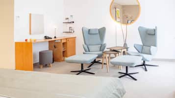 A modern room with a bed, two armchairs, a small table, a desk, and a mirror.