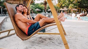 A couple relaxing on a wicker lounge chair by a poolside.