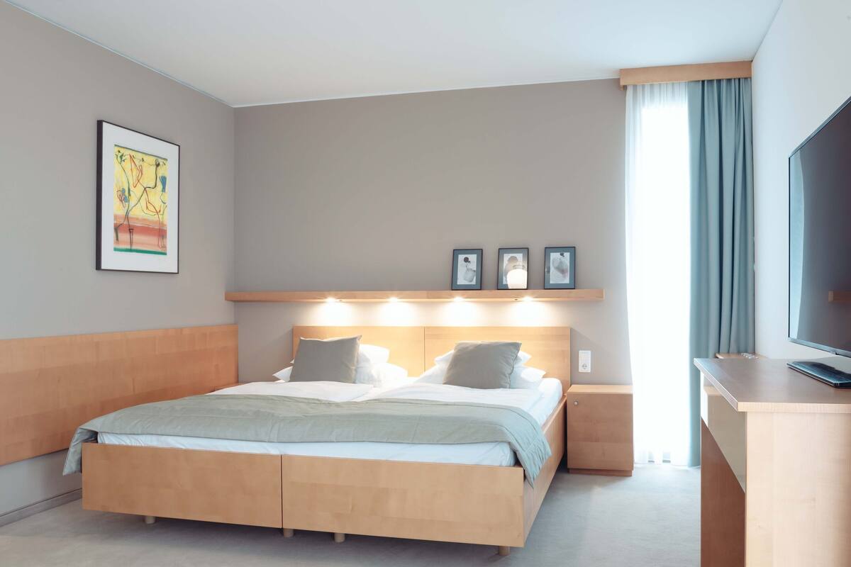 A modern hotel room with a wooden bed, bedside table, and a flat-screen TV.