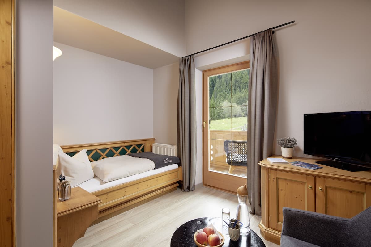 Una habitación acogedora con cama, televisión, una mesita con un frutero y vista a un jardín por la ventana.