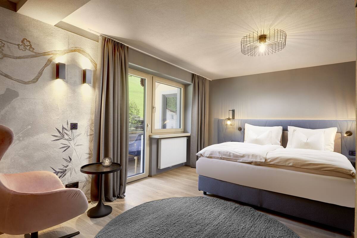 Una habitación de hotel moderna con cama, una silla, una mesita y vistas al exterior.