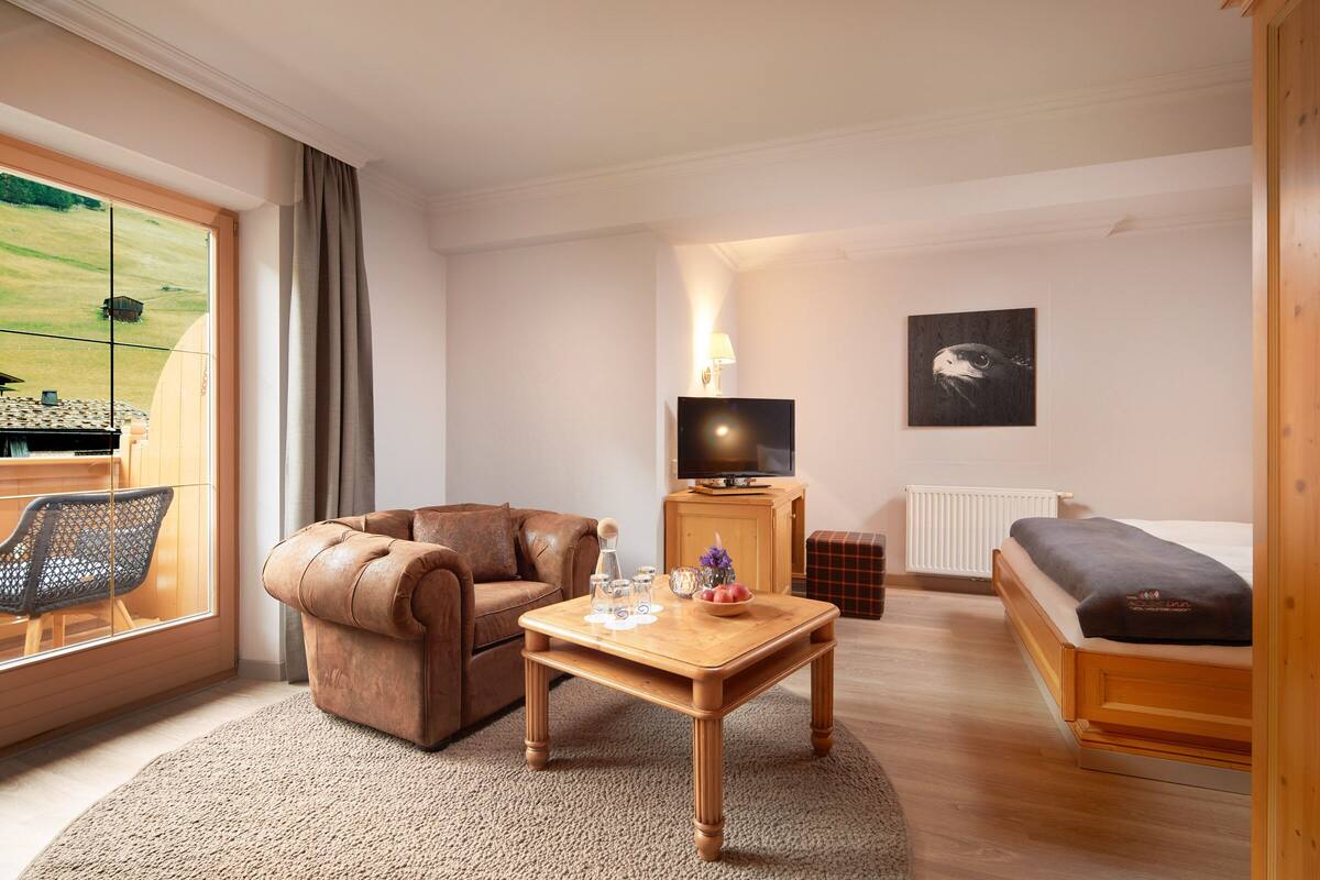 Una sala de estar acogedora con un sofá de cuero, una mesa de centro de madera, un televisor y vistas a un campo verde a través de un ventanal grande.