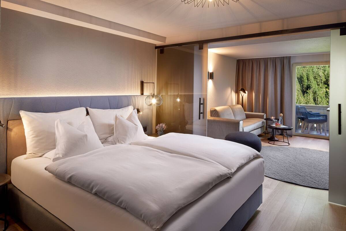 Habitación de hotel moderna con una cama grande, una zona de estar con mesa y vistas a zonas verdes.