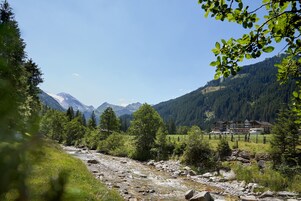 Paisaje montañoso con un río, árboles y un edificio de varios pisos y balcones.